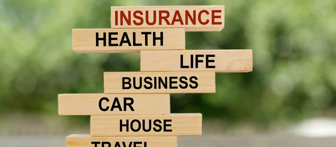 Wooden blocks stacked in a tower labelled with types of insurance, including health, life, business, car and house