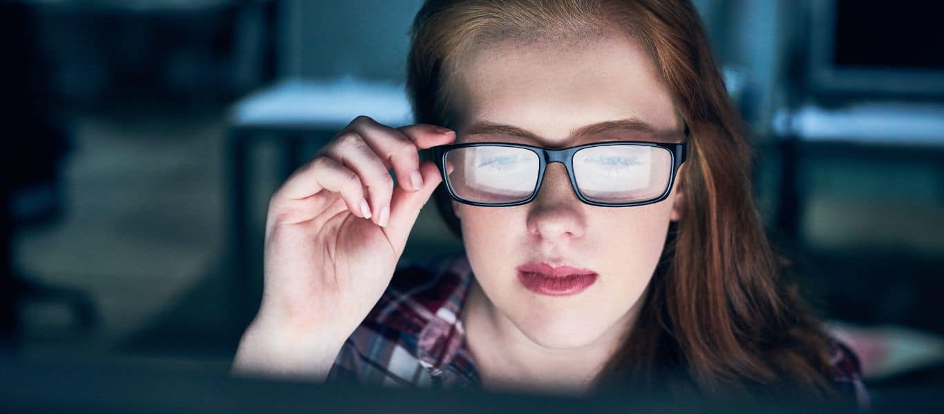 Person adjusting their glasses while reading closely on a computer screen